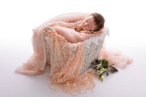 Schlafendes Baby in weißem Korb mit lachsfarbenen Decken
